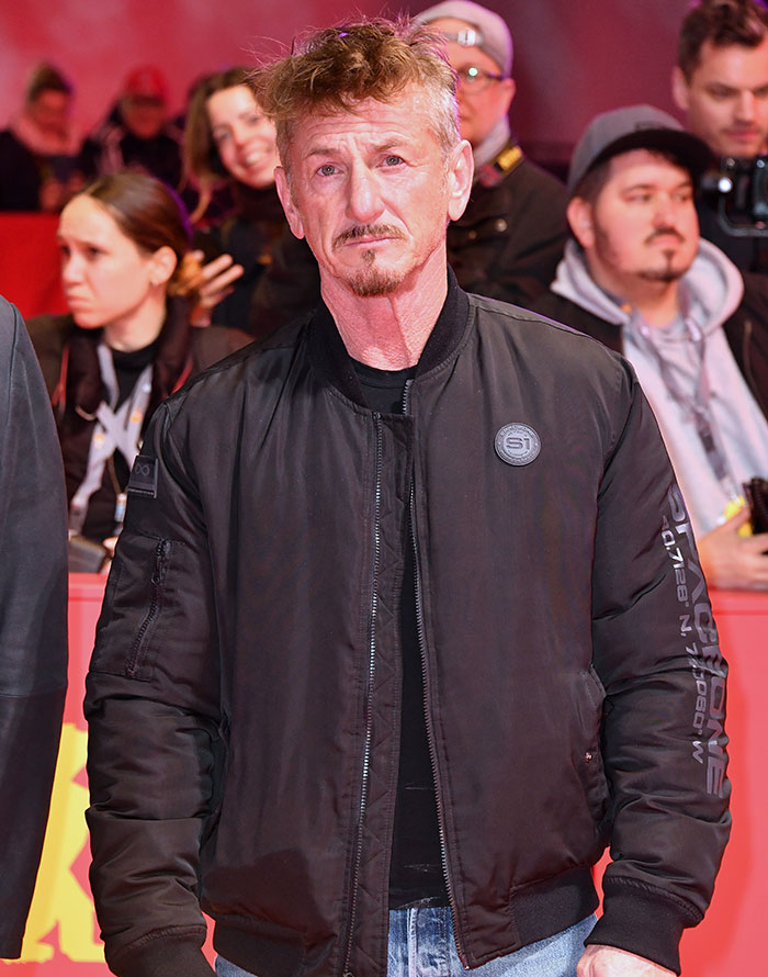 Sean Penn in a black jacket at an event, with people in the background on a red carpet. Sean Penn in a black jacket at an event, with people in the background on a red carpet.