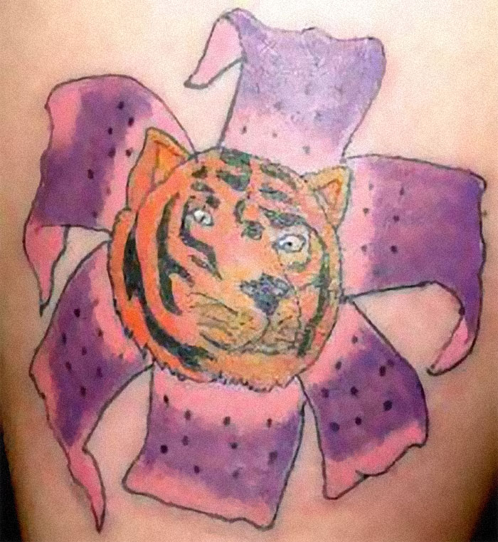 Tattoo fail featuring an awkward tiger face on a purple flower design.