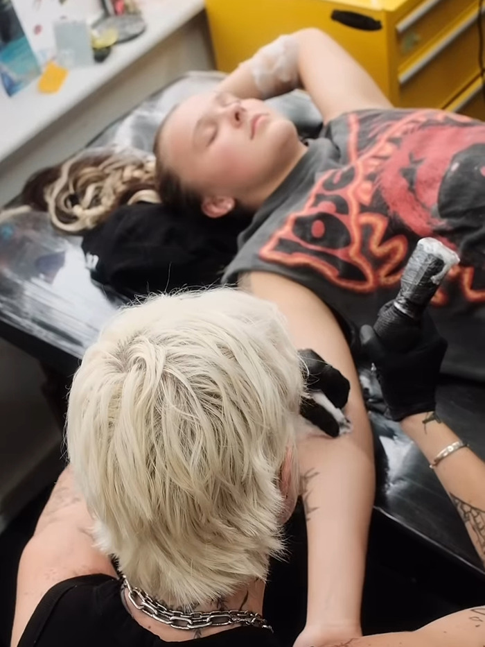 Tattoo artist working on JoJo Siwa's arm, creating new ink in a brightly lit studio. Tattoo artist working on JoJo Siwa's arm, creating new ink in a brightly lit studio.