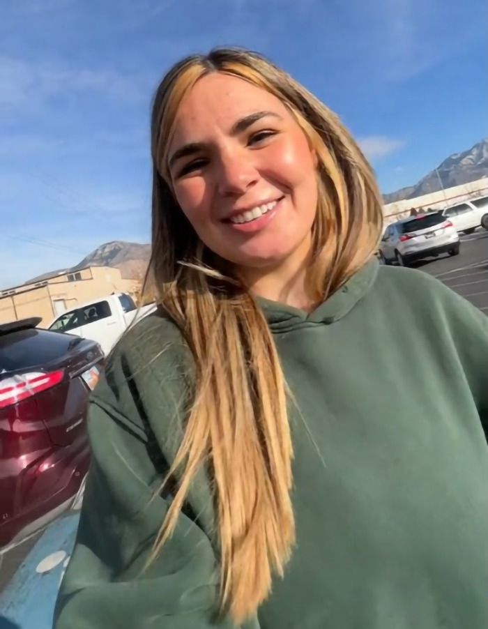 Smiling woman outdoors in a parking lot with mountains in the background, associated with viral momfluencer content. Smiling woman outdoors in a parking lot with mountains in the background, associated with viral momfluencer content.