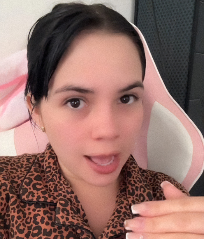 Nebrazkha in leopard print top making a facial expression, seated indoors on a pink chair. Nebrazkha in leopard print top making a facial expression, seated indoors on a pink chair.