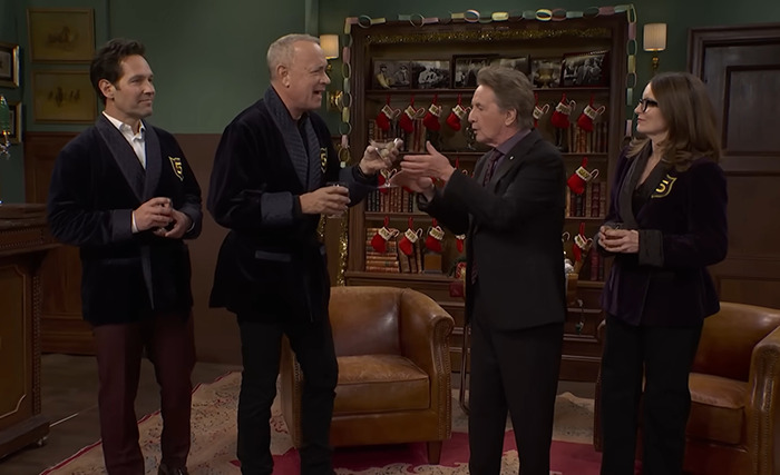Tom Hanks on SNL set, interacting with other cast members, sparking concern among fans about his hands. Tom Hanks on SNL set, interacting with other cast members, sparking concern among fans about his hands.