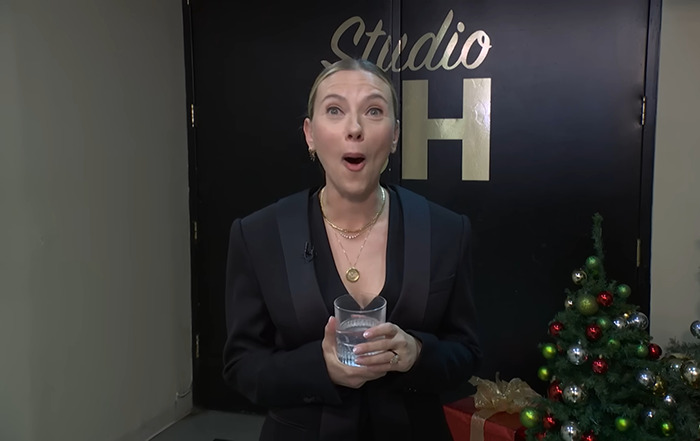 Scarlett Johansson reacts with surprise, holding a glass backstage, standing near a decorated Christmas tree. Scarlett Johansson reacts with surprise, holding a glass backstage, standing near a decorated Christmas tree.