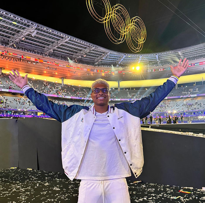 French Olympian celebrating under illuminated rings at Paris 2024 stadium. French Olympian celebrating under illuminated rings at Paris 2024 stadium.