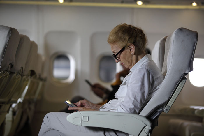 Elderly woman in plane seat using phone, with mobility keywords highlighted in context. Elderly woman in plane seat using phone, with mobility keywords highlighted in context.