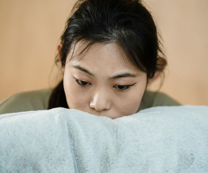 New mom looking pensive in a soft-lit room, resting on a plush cover. Focused expression suggests contemplation. New mom looking pensive in a soft-lit room, resting on a plush cover. Focused expression suggests contemplation.