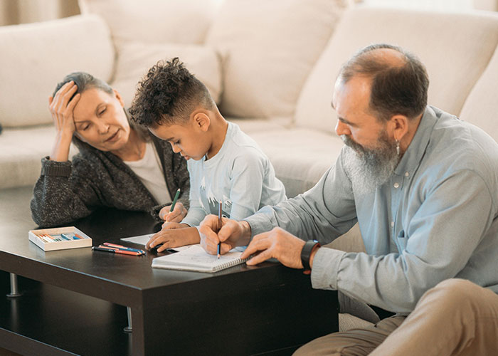 Grandparents and a young boy drawing with colored pencils at a coffee table in a cozy living room. Grandparents and a young boy drawing with colored pencils at a coffee table in a cozy living room.