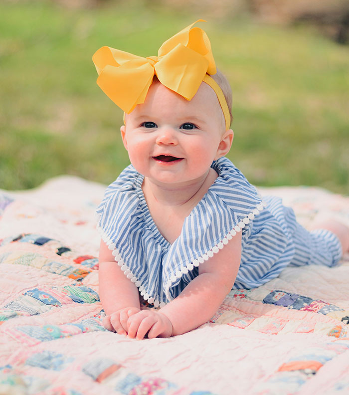 Baby with a yellow bow on a colorful quilt, related to child-free wedding controversy. Baby with a yellow bow on a colorful quilt, related to child-free wedding controversy.