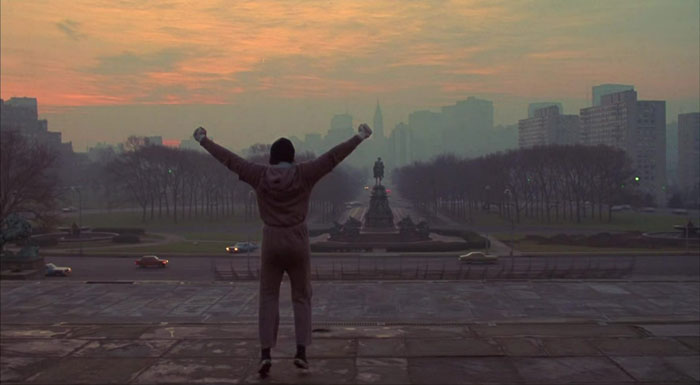 Person posing on steps in a triumphant stance at sunrise, reminiscent of famous Rocky scenes from movies. Person posing on steps in a triumphant stance at sunrise, reminiscent of famous Rocky scenes from movies.