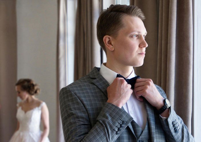 Man adjusting bow tie, preparing for brother wedding engagement, with a bride in white dress in the background. Man adjusting bow tie, preparing for brother wedding engagement, with a bride in white dress in the background.