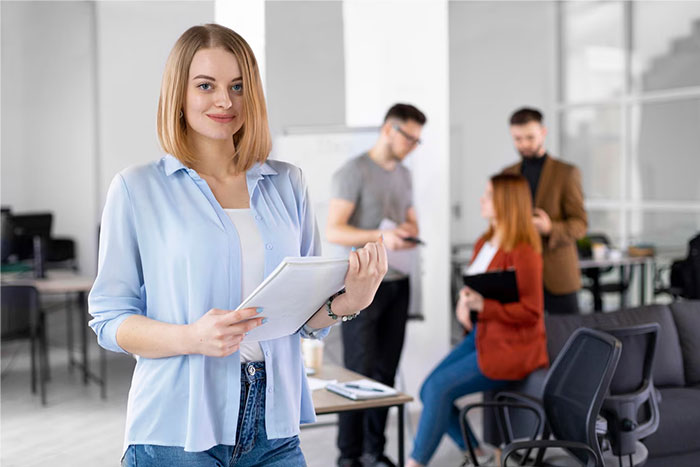 Smiling woman in office setting with colleagues; HR director experiencing stress in the background. Smiling woman in office setting with colleagues; HR director experiencing stress in the background.