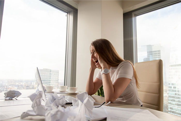 HR Director appearing stressed in an office, surrounded by crumpled papers, looking at a laptop. HR Director appearing stressed in an office, surrounded by crumpled papers, looking at a laptop.