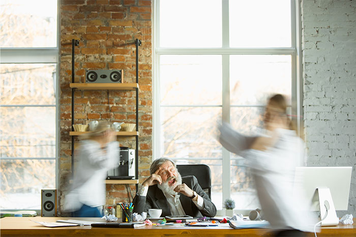 HR director stressed at desk as two colleagues rush past in a busy office setting. HR director stressed at desk as two colleagues rush past in a busy office setting.