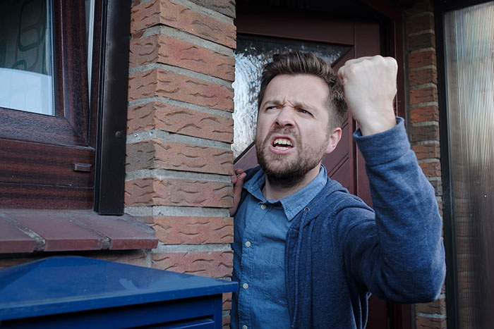 Man frustrated near doorway, raising fist, after neighbors shut off his Wi-Fi. Man frustrated near doorway, raising fist, after neighbors shut off his Wi-Fi.