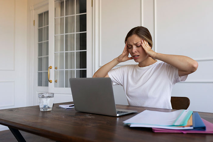 A woman sitting at a table with a laptop, appearing stressed over shut off Wi-Fi, in a room with white walls and glass doors. A woman sitting at a table with a laptop, appearing stressed over shut off Wi-Fi, in a room with white walls and glass doors.
