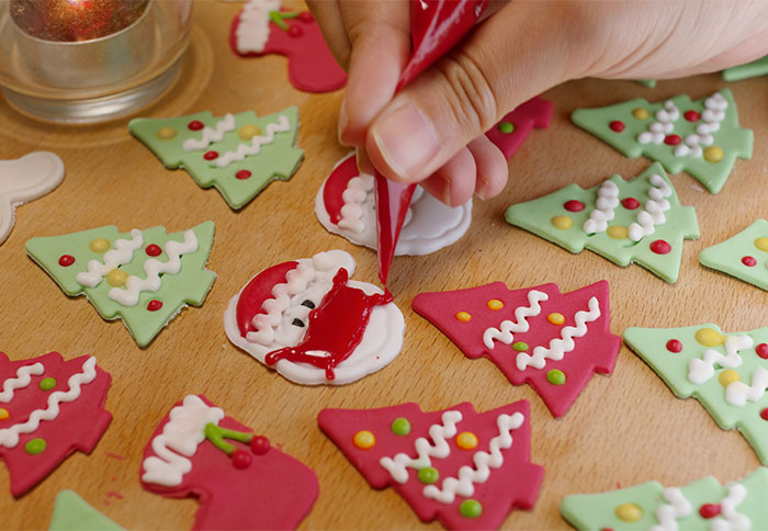 Hand decorating Christmas cookies with icing on a wooden table, featuring festive tree and Santa designs. Hand decorating Christmas cookies with icing on a wooden table, featuring festive tree and Santa designs.