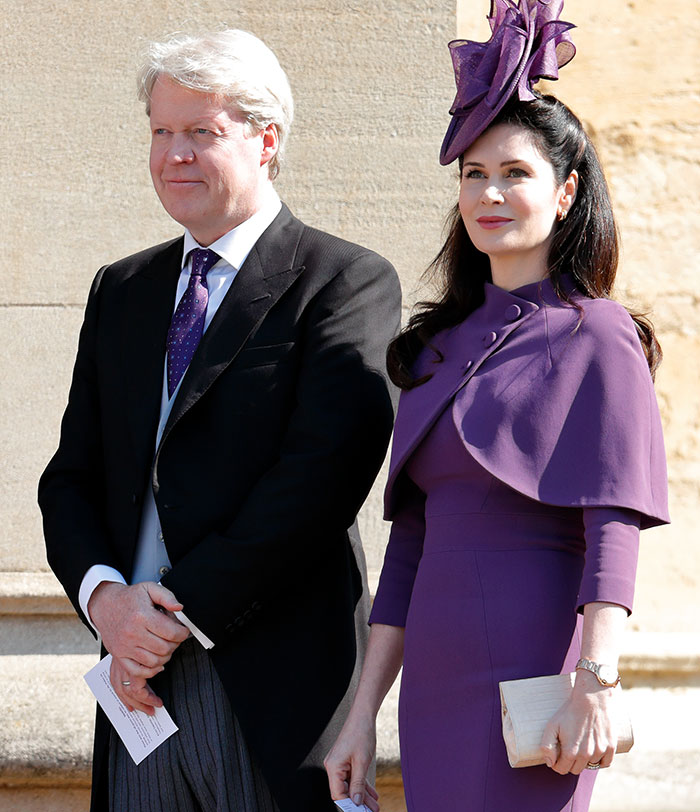 A man in a suit and a woman in a purple outfit with a matching hat, standing outdoors at an event. A man in a suit and a woman in a purple outfit with a matching hat, standing outdoors at an event.