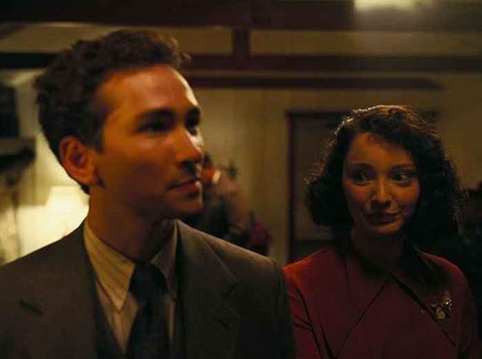 Emma Dumont in period attire, engaging with a man in a dimly lit room, showcasing a vintage ambiance. Emma Dumont in period attire, engaging with a man in a dimly lit room, showcasing a vintage ambiance.