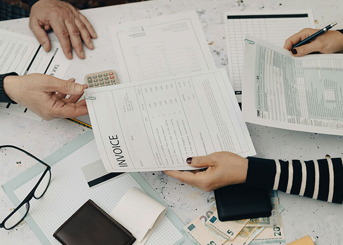 Hands holding invoices and documents over a table with cash and a calculator, illustrating employer demands for overpayment. Hands holding invoices and documents over a table with cash and a calculator, illustrating employer demands for overpayment.