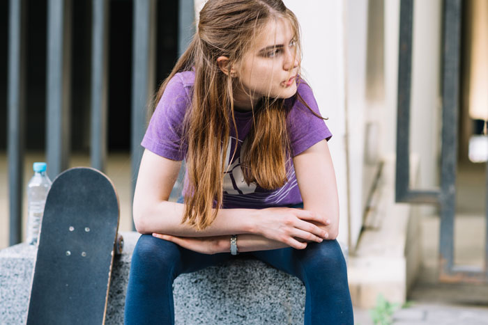 Young woman in a purple shirt sitting with a skateboard nearby, appearing thoughtful. Young woman in a purple shirt sitting with a skateboard nearby, appearing thoughtful.