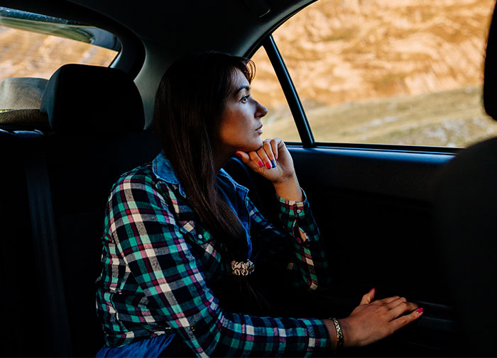 Woman in a checkered shirt sitting thoughtfully in a car, looking out the window, relating to a fiance demanding to sell the car. Woman in a checkered shirt sitting thoughtfully in a car, looking out the window, relating to a fiance demanding to sell the car.