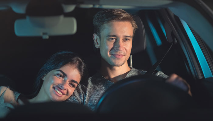Couple smiling in a car at night, planning a surprise house prank. Couple smiling in a car at night, planning a surprise house prank.