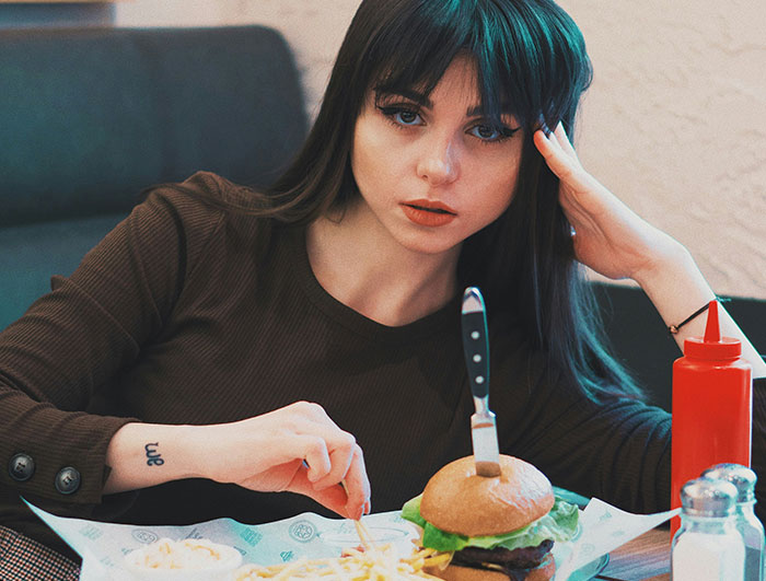 Woman sitting at a table with a hamburger and fries, looking frustrated, highlighting friend always late issue. Woman sitting at a table with a hamburger and fries, looking frustrated, highlighting friend always late issue.