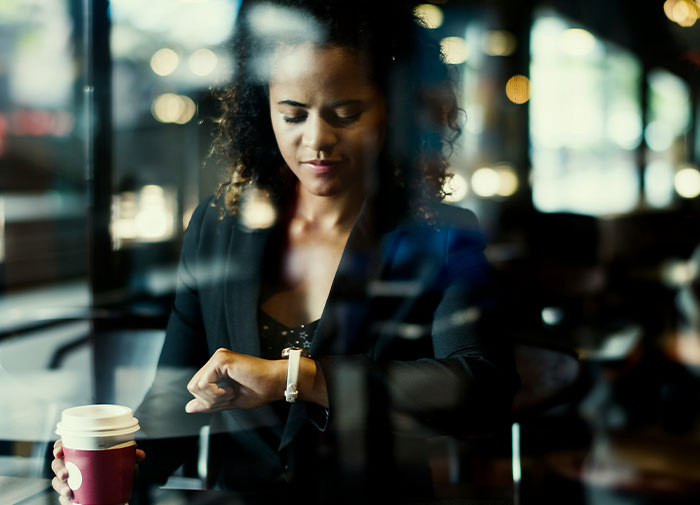 Woman checking watch, holding coffee cup, seemingly frustrated by friend always being late. Woman checking watch, holding coffee cup, seemingly frustrated by friend always being late.