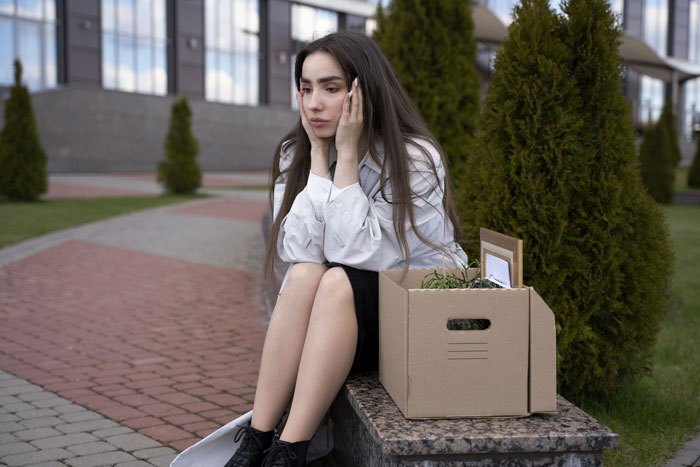 Woman sitting on a bench with a cardboard box, looking regretful after rejecting proposal. Woman sitting on a bench with a cardboard box, looking regretful after rejecting proposal.