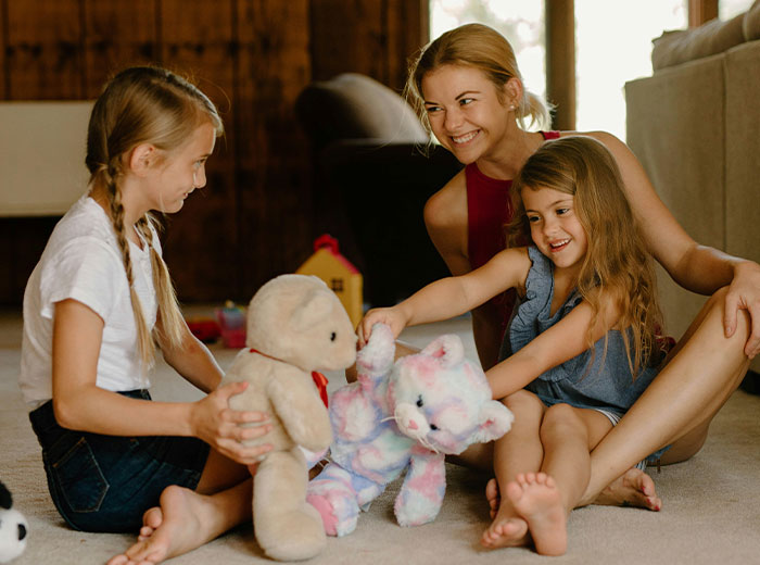 Mother and daughters playing with stuffed animals in a cozy living room. Mother and daughters playing with stuffed animals in a cozy living room.
