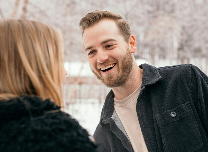 A man smiling at a woman outdoors, expressing happiness in a snowy setting, related to family discussions and relationships. A man smiling at a woman outdoors, expressing happiness in a snowy setting, related to family discussions and relationships.