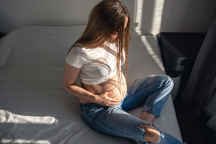 Pregnant woman sitting on a bed, holding her belly, contemplating baby names. Pregnant woman sitting on a bed, holding her belly, contemplating baby names.