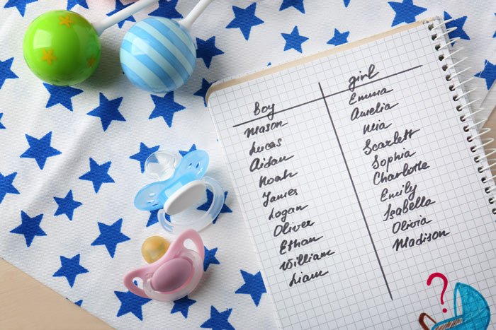 Notebook with baby names list next to pacifiers and baby toys on a star-patterned cloth. Notebook with baby names list next to pacifiers and baby toys on a star-patterned cloth.