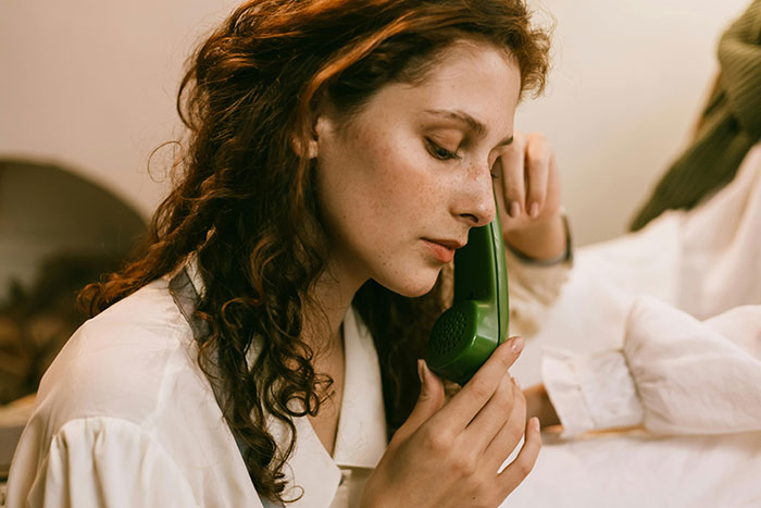 A woman in a white blouse, holding a retro green phone to her ear indoors. A woman in a white blouse, holding a retro green phone to her ear indoors.