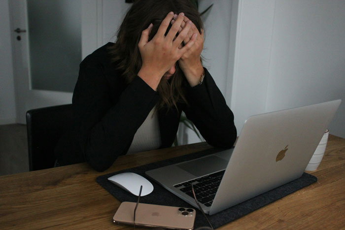 A frustrated woman at a desk with a laptop, holding her head during a critical job test. A frustrated woman at a desk with a laptop, holding her head during a critical job test.