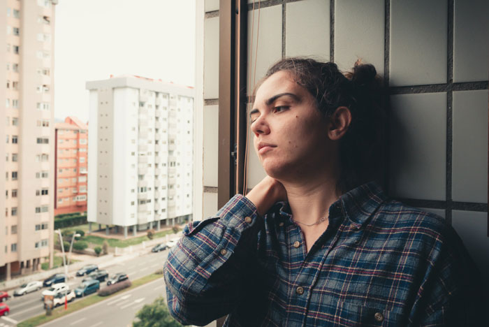 Woman looking frustrated by a window, wearing a plaid shirt, contemplating after an interruption during her job test. Woman looking frustrated by a window, wearing a plaid shirt, contemplating after an interruption during her job test.
