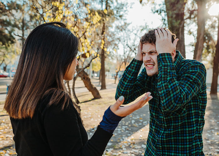 A couple arguing in a park, with the husband looking defensive, wearing a green plaid shirt. A couple arguing in a park, with the husband looking defensive, wearing a green plaid shirt.