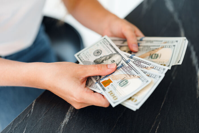 Hands holding several hundred-dollar bills on a dark marble table. Hands holding several hundred-dollar bills on a dark marble table.