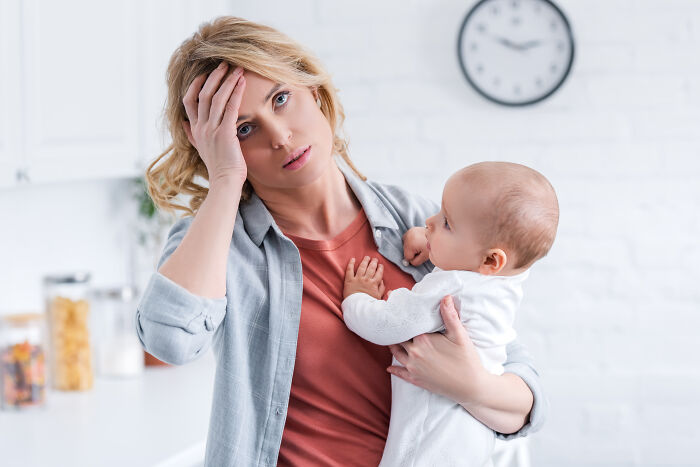 Woman holding a baby, looking stressed, in a bright kitchen setting. Woman holding a baby, looking stressed, in a bright kitchen setting.
