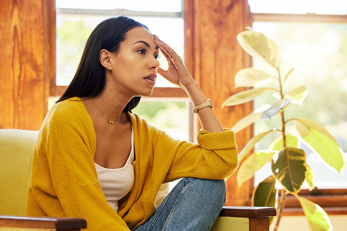 Woman feeling upset about husband's "work wife," sitting by window, wearing yellow cardigan. Woman feeling upset about husband's "work wife," sitting by window, wearing yellow cardigan.