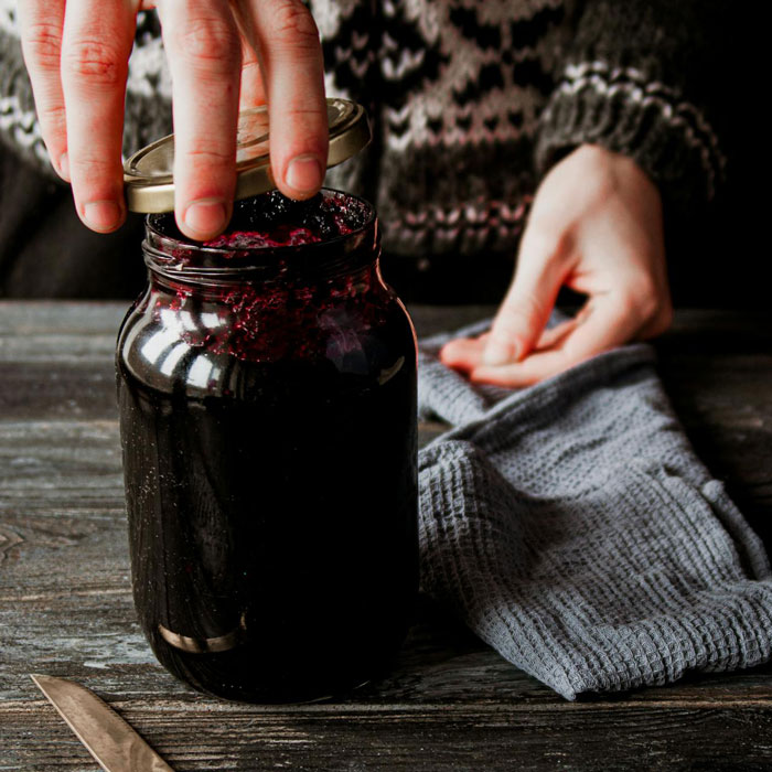 Woman's hands sealing a jar of jam on a wooden table, with a grey cloth beside it. Woman's hands sealing a jar of jam on a wooden table, with a grey cloth beside it.