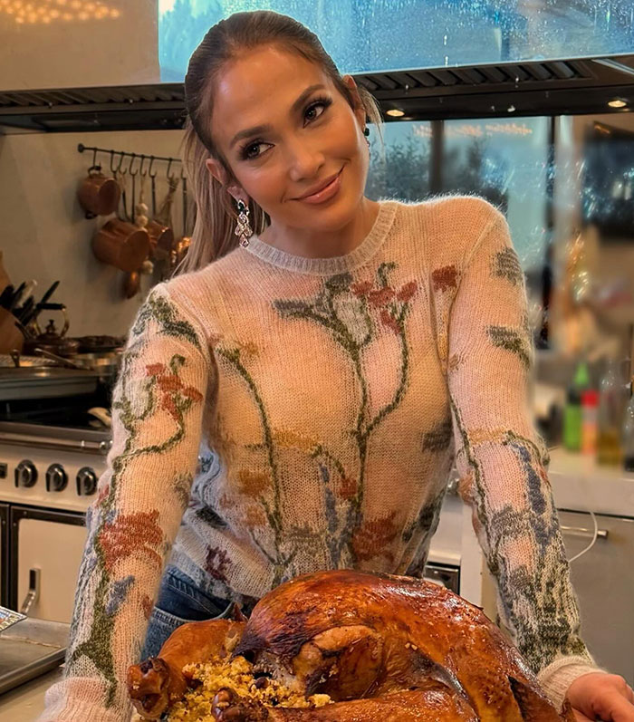 Jennifer Lopez in a kitchen with a floral sweater, leaning on a counter with a roasted turkey. Jennifer Lopez in a kitchen with a floral sweater, leaning on a counter with a roasted turkey.