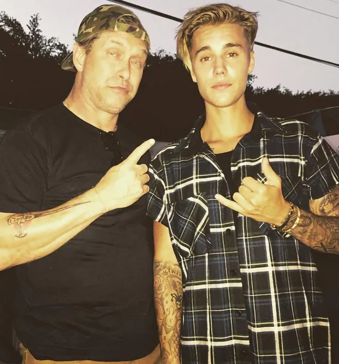 Stephen Baldwin with son-in-law Justin Bieber, both making hand gestures, amidst a backdrop of trees and wire. Stephen Baldwin with son-in-law Justin Bieber, both making hand gestures, amidst a backdrop of trees and wire.