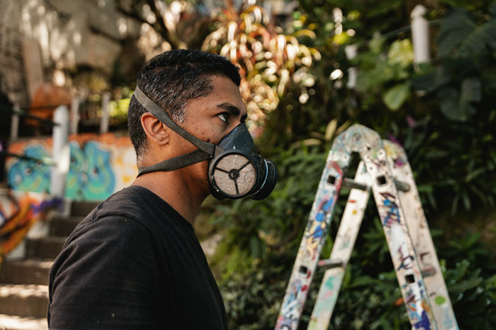 Man wearing a mask outdoors with graffiti and ladder in background, highlighting mask-wearing context. Man wearing a mask outdoors with graffiti and ladder in background, highlighting mask-wearing context.
