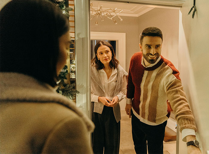 "Couple at door greeting guest, preparing for petty revenge in holiday setting. "Couple at door greeting guest, preparing for petty revenge in holiday setting.