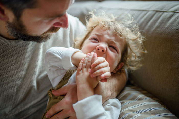 A man comforting a distressed child on a couch, emphasizing family dynamics. A man comforting a distressed child on a couch, emphasizing family dynamics.