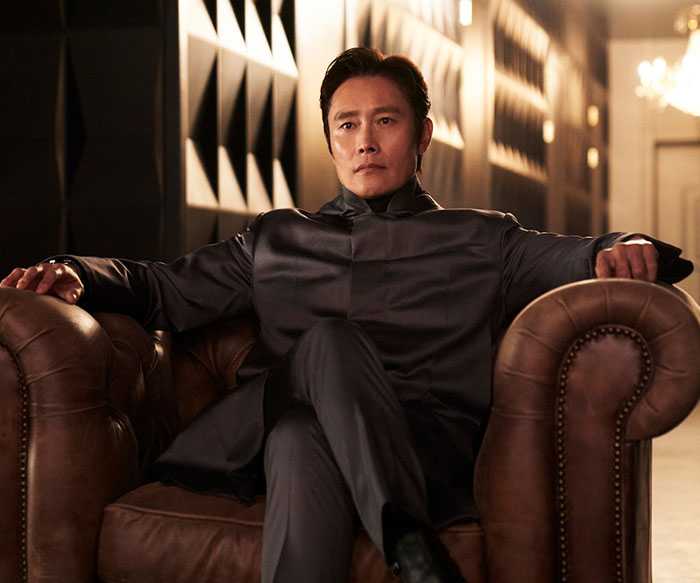 Actor in a black suit sitting on a leather chair, related to "Squid Game 2" cast controversies. Actor in a black suit sitting on a leather chair, related to "Squid Game 2" cast controversies.