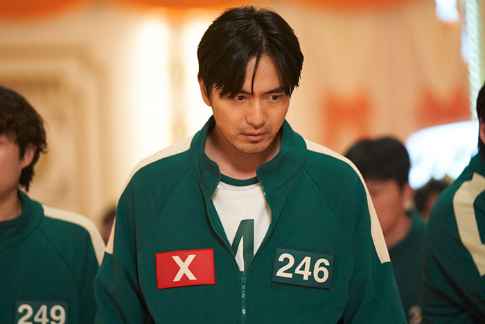 Cast member in green track jacket with number 246 from Squid Game 2, amidst controversy and fan backlash. Cast member in green track jacket with number 246 from Squid Game 2, amidst controversy and fan backlash.