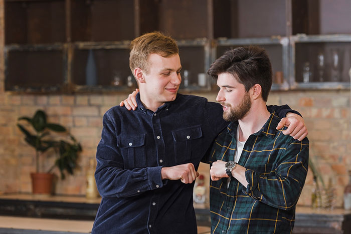 Two friends in casual shirts bumping elbows in a cozy kitchen setting, highlighting a moment of friendship. Two friends in casual shirts bumping elbows in a cozy kitchen setting, highlighting a moment of friendship.