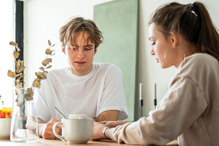 Young man discussing family dynamics with woman at a table, addressing assumptions about his sexuality. Young man discussing family dynamics with woman at a table, addressing assumptions about his sexuality.